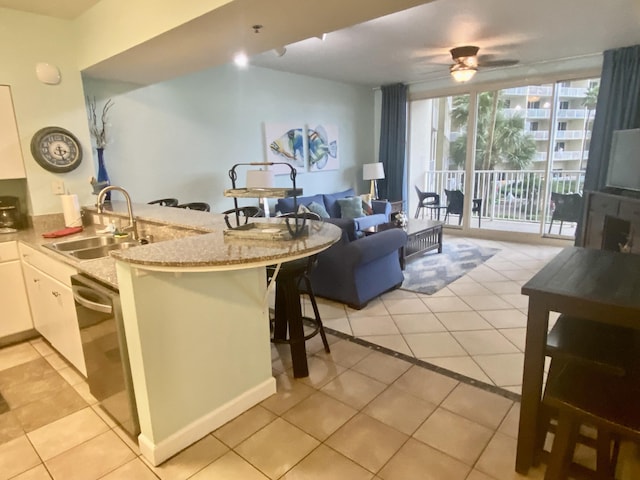 kitchen with a breakfast bar area, kitchen peninsula, light tile patterned floors, white cabinets, and sink