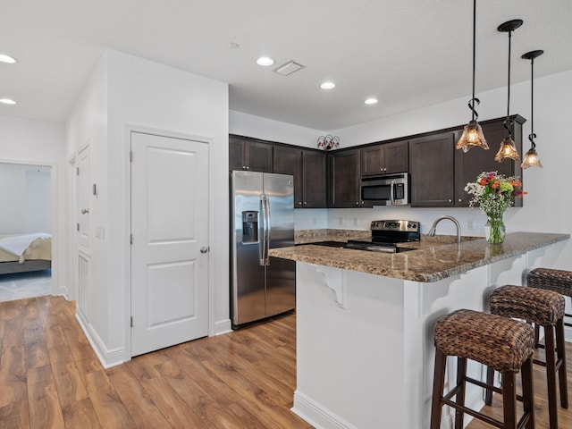 kitchen with a breakfast bar area, dark stone countertops, hanging light fixtures, dark brown cabinets, and stainless steel appliances