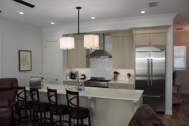 kitchen with range, built in fridge, pendant lighting, a kitchen island with sink, and wall chimney range hood