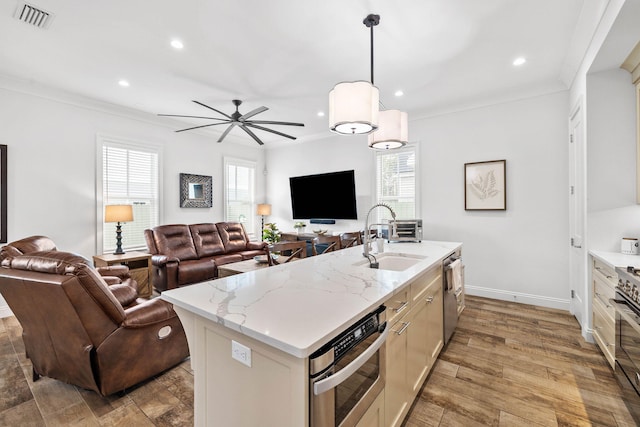 kitchen featuring appliances with stainless steel finishes, sink, hanging light fixtures, ornamental molding, and a center island with sink