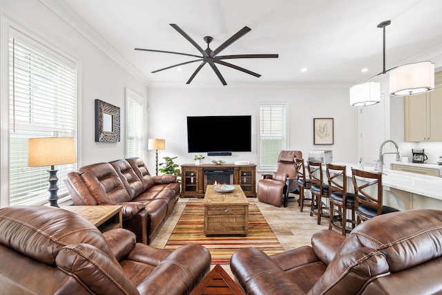 living room with sink, crown molding, light hardwood / wood-style flooring, and ceiling fan