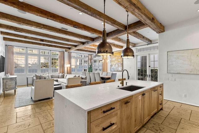 kitchen with sink, pendant lighting, light brown cabinets, a center island with sink, and beam ceiling