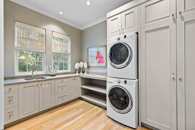 laundry room featuring cabinets, sink, stacked washing maching and dryer, light wood-type flooring, and ornamental molding