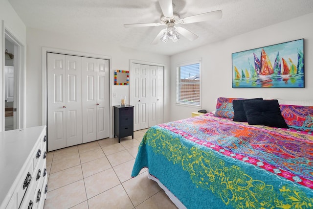 tiled bedroom featuring a textured ceiling, ceiling fan, and multiple closets