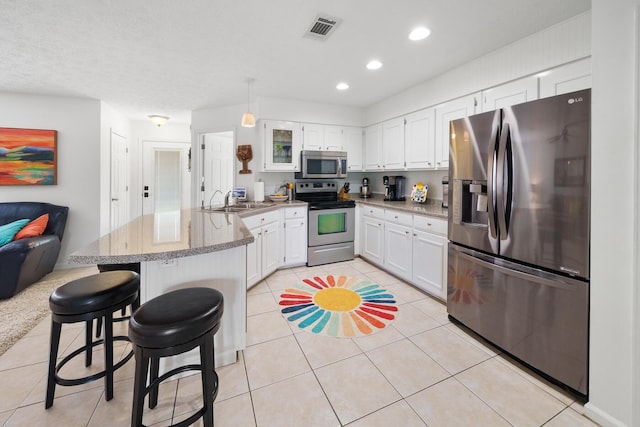 kitchen with a kitchen bar, white cabinets, light tile patterned flooring, and appliances with stainless steel finishes