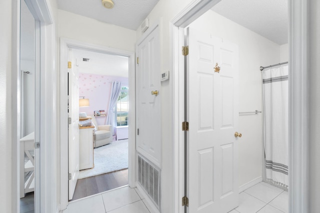 hallway with a textured ceiling and light tile patterned floors