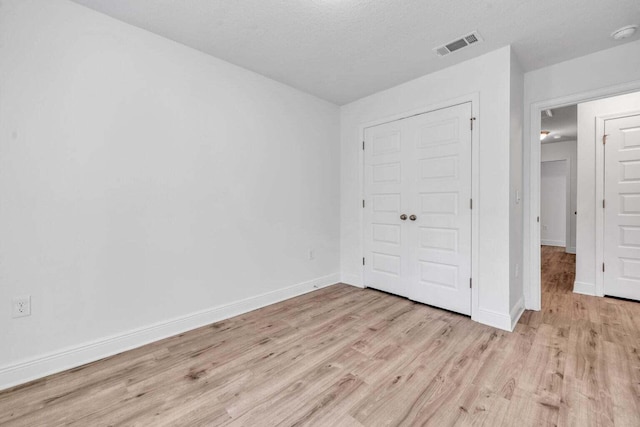 unfurnished bedroom featuring light hardwood / wood-style floors, a textured ceiling, and a closet