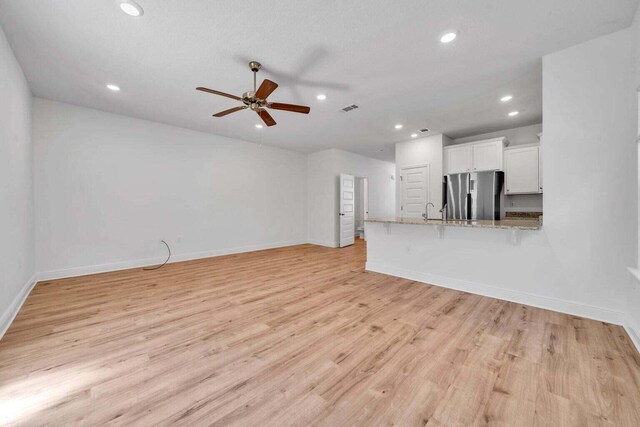 unfurnished living room featuring light hardwood / wood-style floors, ceiling fan, and sink