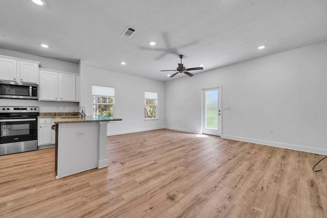 kitchen with white cabinetry, dark stone countertops, light hardwood / wood-style floors, a textured ceiling, and range