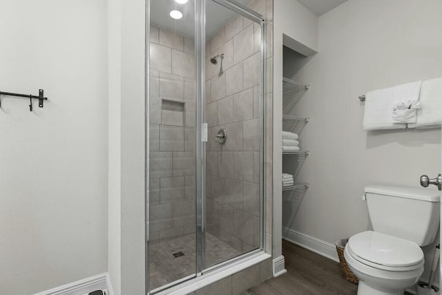 bathroom with wood-type flooring, a shower with shower door, and toilet