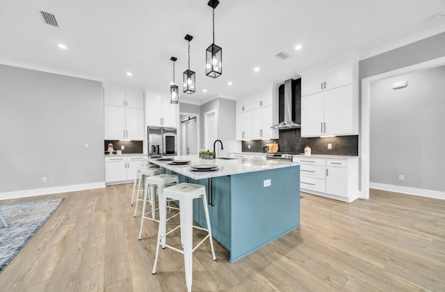 kitchen featuring appliances with stainless steel finishes, white cabinetry, a spacious island, and wall chimney range hood