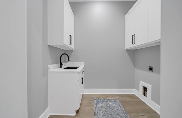 laundry room with electric dryer hookup, sink, cabinets, and light wood-type flooring