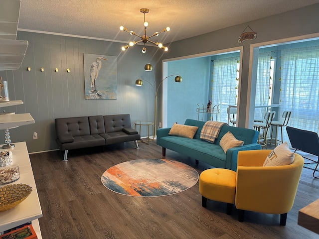 living room featuring ornamental molding, a textured ceiling, dark wood-type flooring, a chandelier, and wood walls