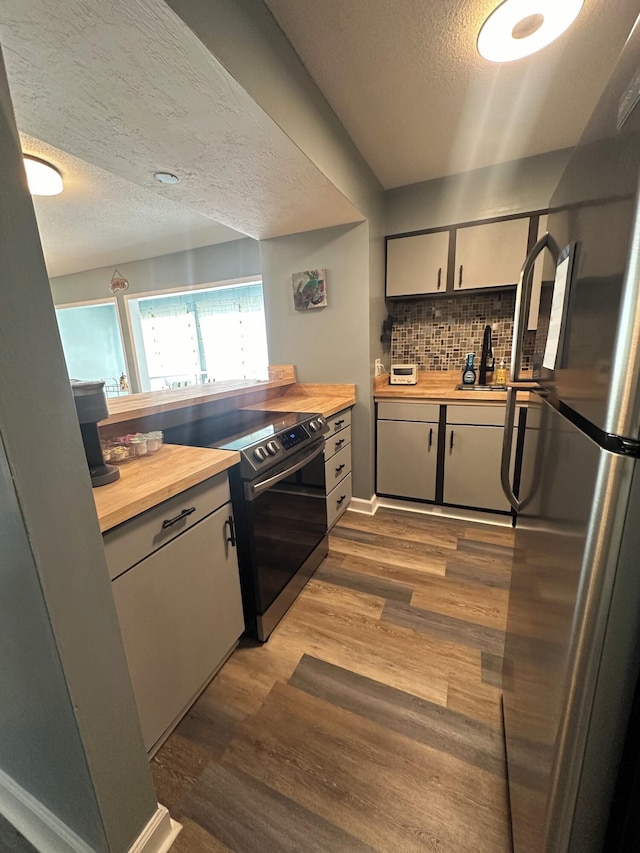 kitchen with decorative backsplash, dark hardwood / wood-style flooring, a textured ceiling, butcher block countertops, and range with electric stovetop