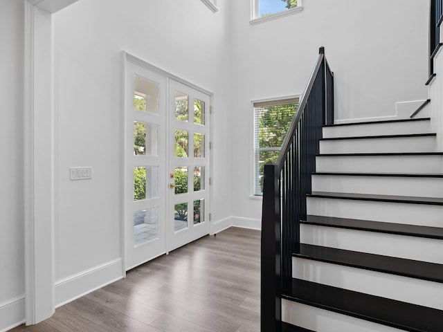 entryway with french doors, a towering ceiling, wood finished floors, baseboards, and stairs