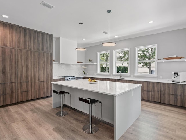 kitchen with a kitchen island, a breakfast bar, sink, backsplash, and light hardwood / wood-style floors