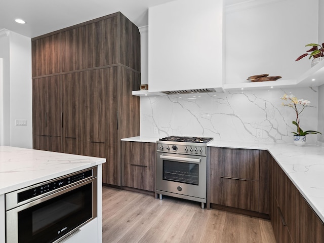 kitchen featuring high end range, tasteful backsplash, light hardwood / wood-style floors, and oven