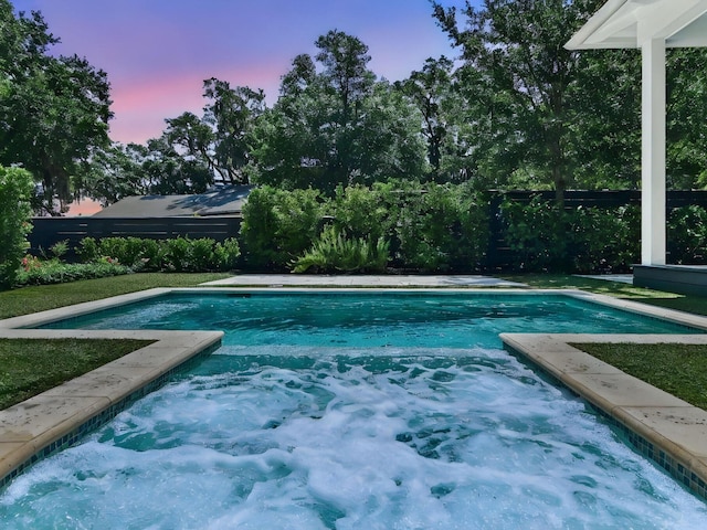 pool at dusk with an outdoor pool and fence