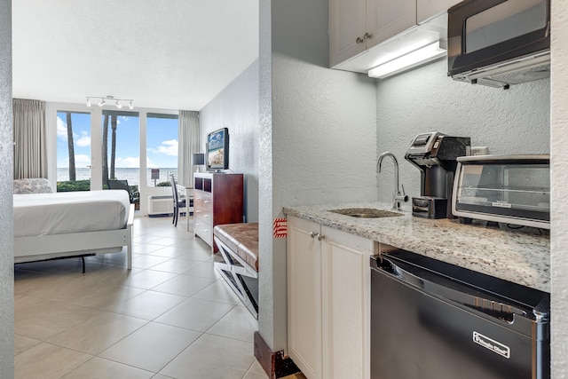 kitchen with track lighting, black dishwasher, sink, light stone counters, and light tile patterned floors