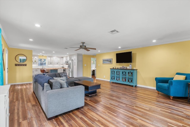 living room featuring ceiling fan, crown molding, and light hardwood / wood-style flooring