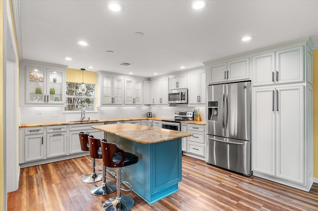 kitchen with a kitchen breakfast bar, appliances with stainless steel finishes, a center island, white cabinetry, and decorative light fixtures