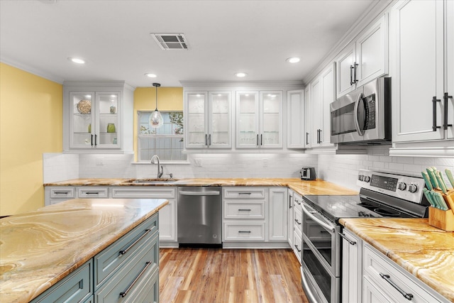 kitchen featuring stainless steel appliances, sink, white cabinets, light hardwood / wood-style floors, and hanging light fixtures