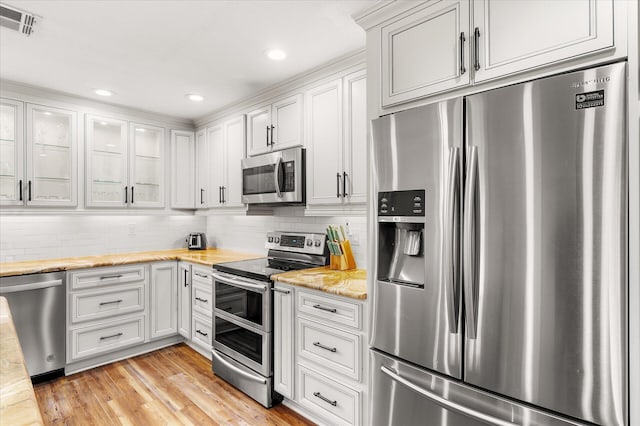 kitchen with appliances with stainless steel finishes, light hardwood / wood-style floors, light stone countertops, decorative backsplash, and white cabinets