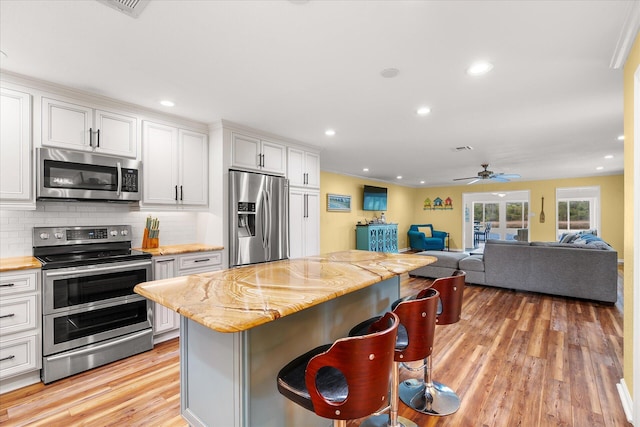 kitchen with a kitchen bar, appliances with stainless steel finishes, ceiling fan, and white cabinetry