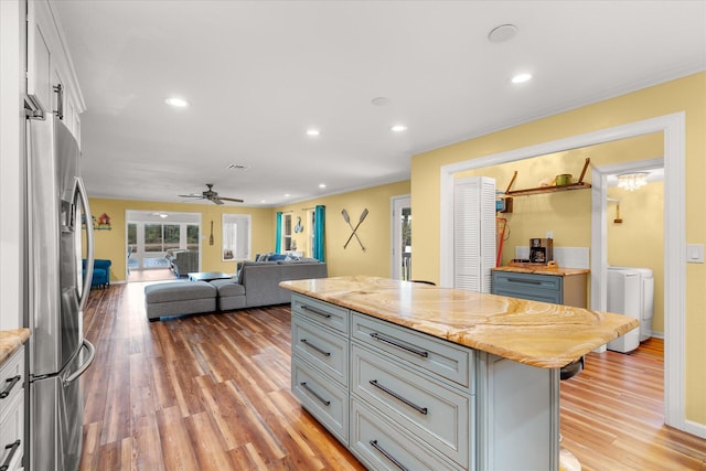 kitchen with stainless steel refrigerator, ceiling fan, light stone counters, a kitchen island, and washing machine and clothes dryer