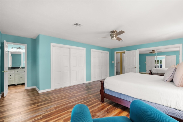 bedroom with connected bathroom, hardwood / wood-style floors, two closets, and ceiling fan