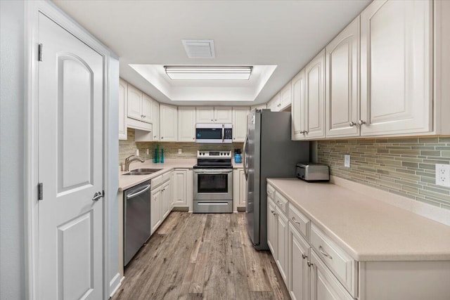 kitchen with stainless steel appliances, a raised ceiling, white cabinetry, and light hardwood / wood-style floors