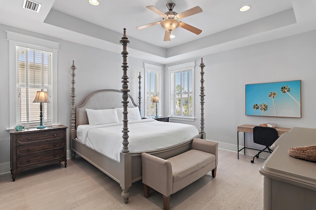 bedroom with a tray ceiling, light wood-type flooring, and visible vents