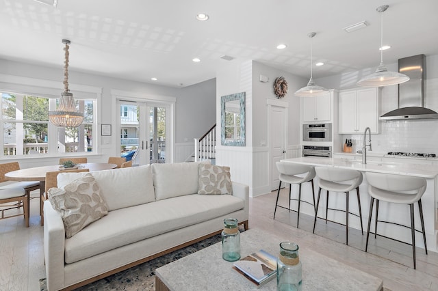 living room with light wood-style flooring, recessed lighting, french doors, stairway, and wainscoting