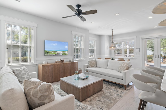 living area featuring a wainscoted wall, french doors, light wood finished floors, and a healthy amount of sunlight