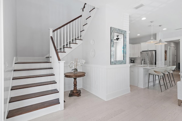 stairs with recessed lighting, visible vents, wood finished floors, and wainscoting