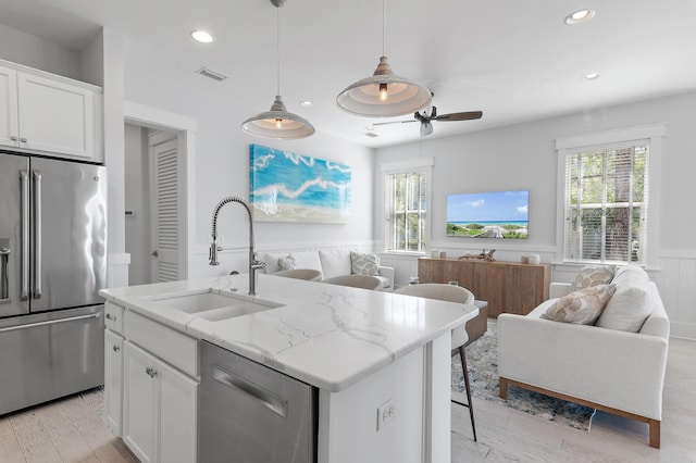 kitchen featuring open floor plan, appliances with stainless steel finishes, a wainscoted wall, and a sink