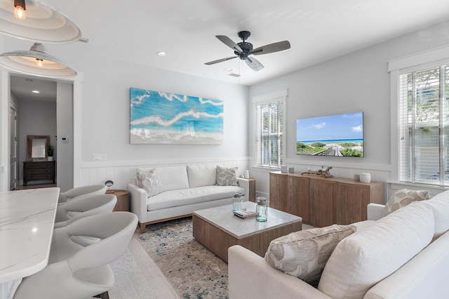 living area featuring a healthy amount of sunlight, a wainscoted wall, ceiling fan, and wood finished floors