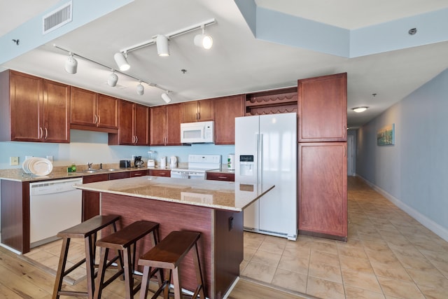 kitchen featuring white appliances, light tile patterned floors, light stone counters, a kitchen island, and a kitchen bar