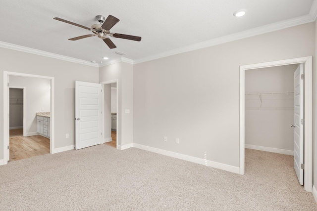 unfurnished bedroom featuring light colored carpet, ceiling fan, ornamental molding, a walk in closet, and ensuite bathroom