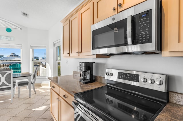 kitchen featuring stainless steel appliances, dark stone counters, light brown cabinetry, a textured ceiling, and light tile patterned flooring