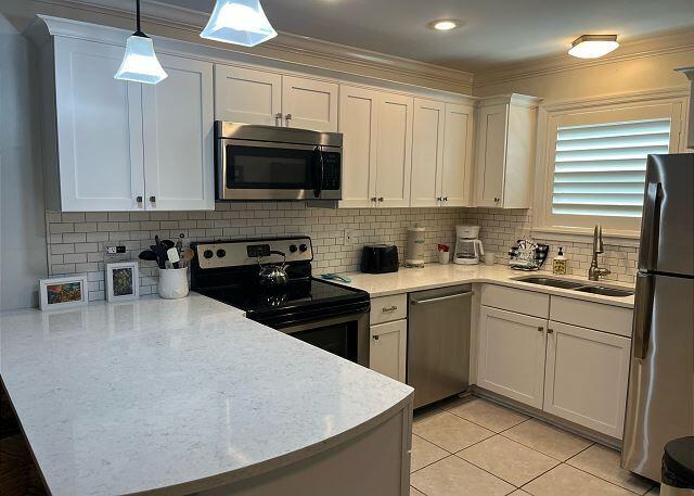 kitchen featuring hanging light fixtures, stainless steel appliances, light tile patterned floors, white cabinets, and sink