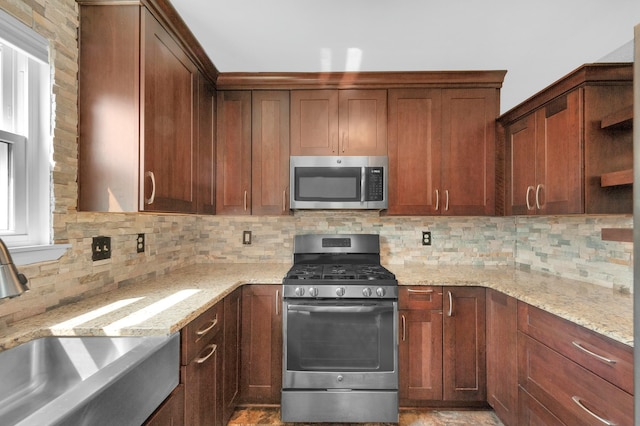 kitchen with sink, backsplash, light stone counters, and appliances with stainless steel finishes