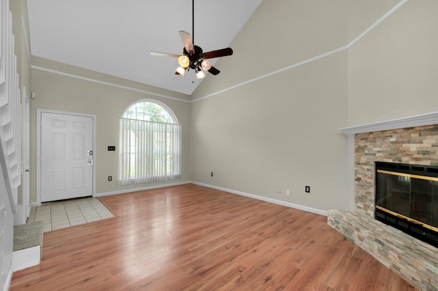 unfurnished living room with ceiling fan, light wood-type flooring, a stone fireplace, and high vaulted ceiling