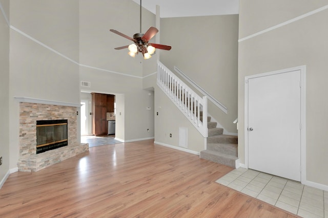 unfurnished living room featuring a high ceiling, ceiling fan, light wood-type flooring, and a stone fireplace