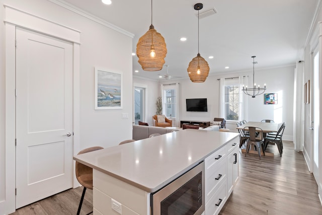 kitchen featuring pendant lighting, built in microwave, a breakfast bar, and white cabinets