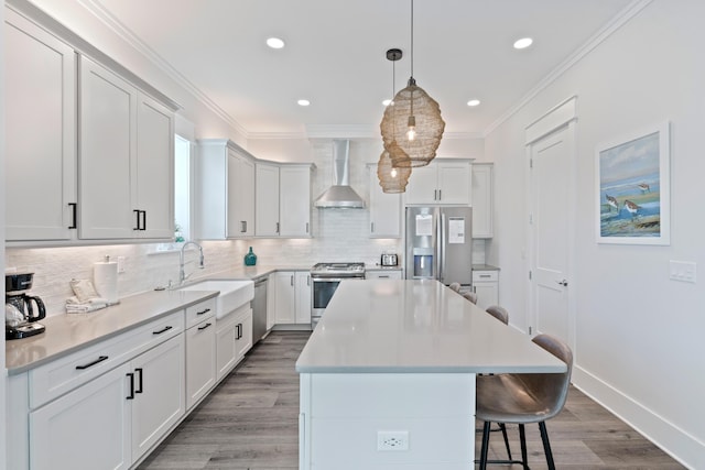 kitchen with a kitchen island, appliances with stainless steel finishes, sink, white cabinets, and wall chimney range hood