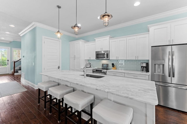 kitchen with appliances with stainless steel finishes, an island with sink, pendant lighting, sink, and white cabinetry