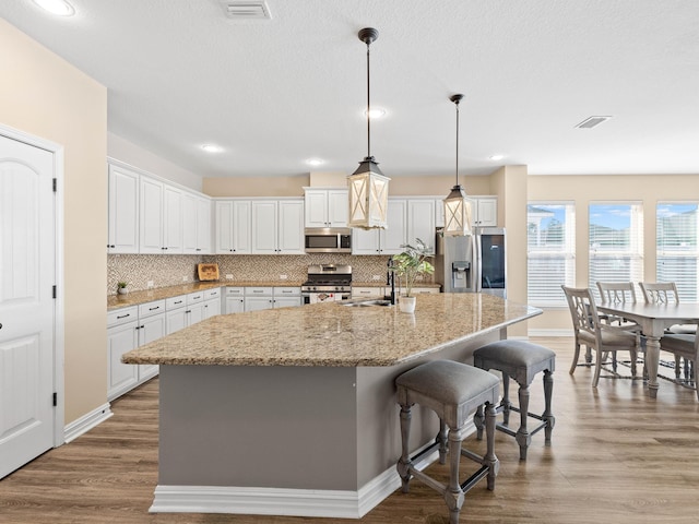 kitchen with stainless steel appliances, a center island with sink, white cabinets, and sink