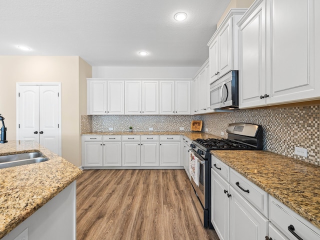 kitchen featuring stainless steel appliances, light stone counters, white cabinets, light hardwood / wood-style flooring, and sink