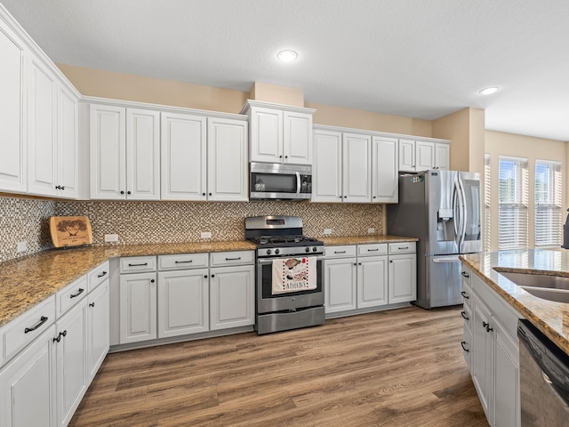 kitchen featuring white cabinets, hardwood / wood-style floors, backsplash, and appliances with stainless steel finishes